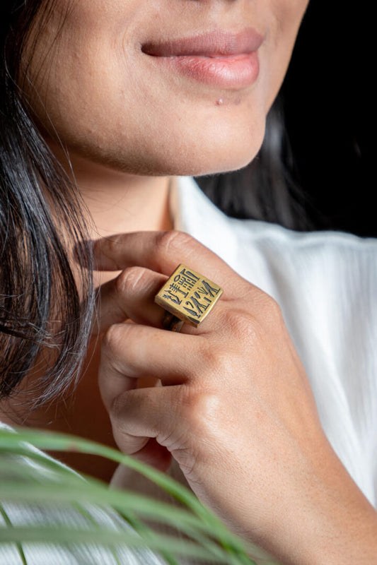 A person wearing a gold-colored brass ring with an ancient Egyptian square design.