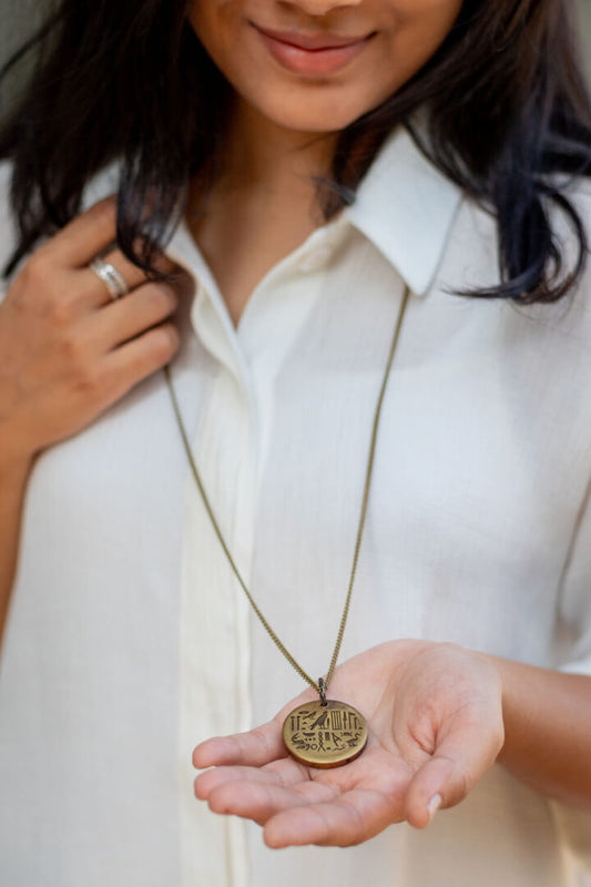 A person wearing a white shirt is holding a brass disc neckpiece with an embossed design.