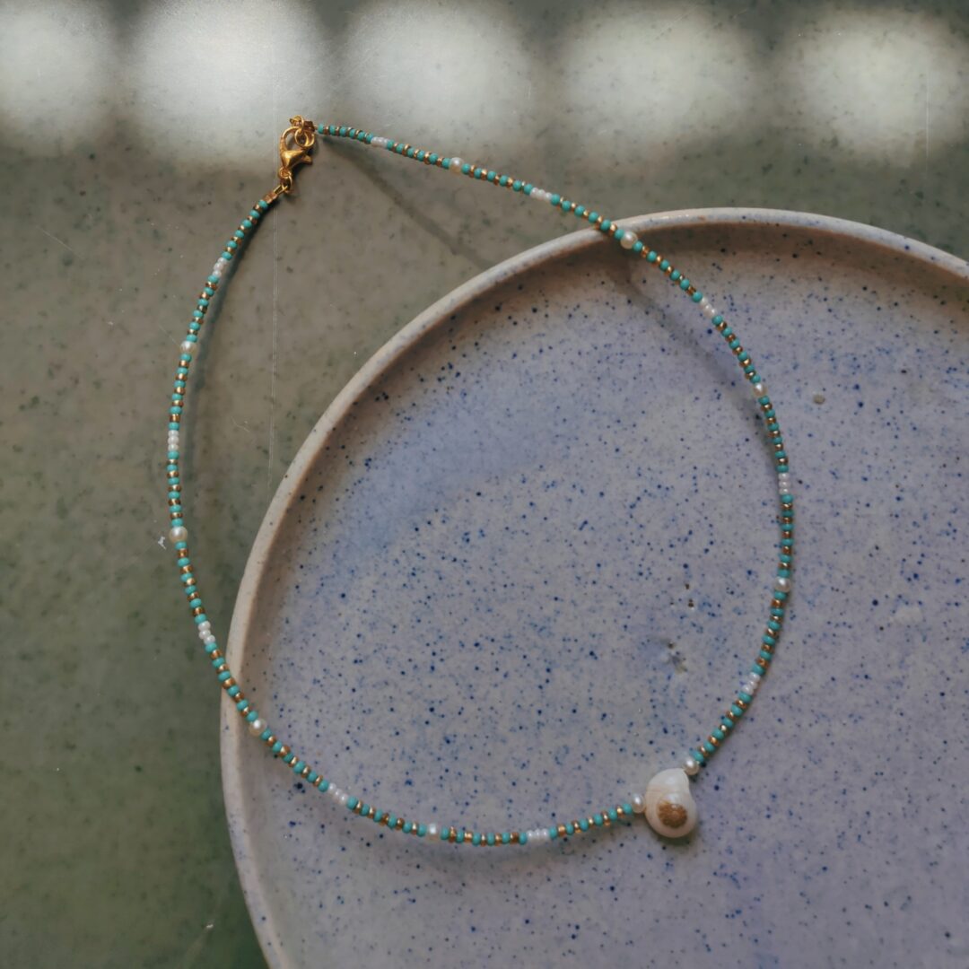 A turquoise beaded necklace with white pearl accents and a shell-like pattern, displayed on a textured background.
