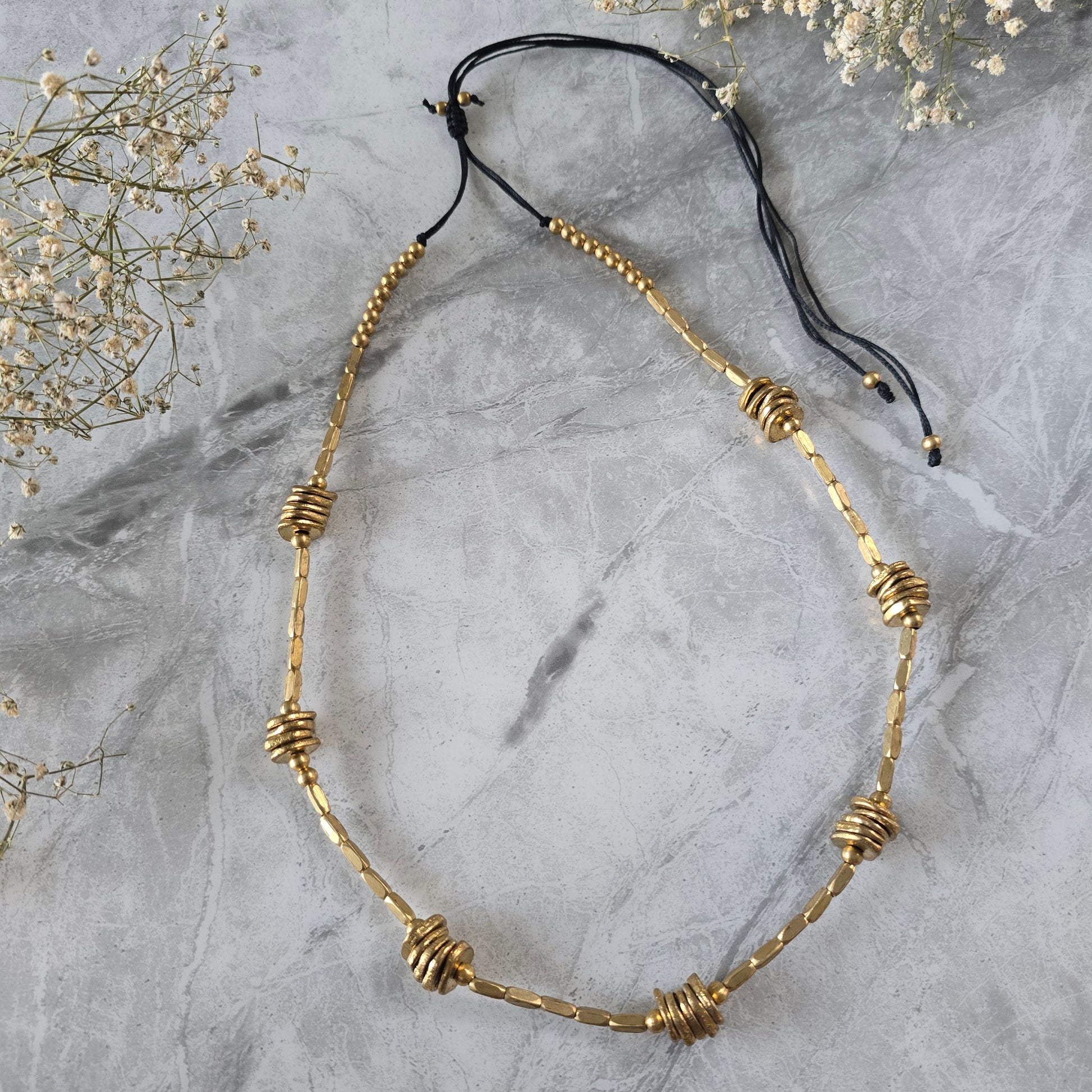 Brass beaded necklace on a gray marble surface with small white flowers.