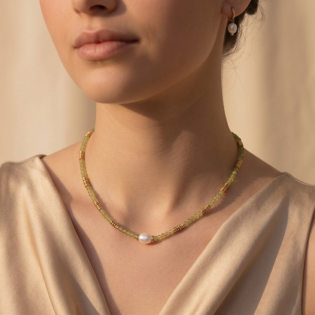 Close-up of a woman wearing a delicate gold necklace with a pearl pendant against a neutral background.