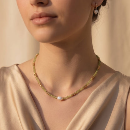 Close-up of a woman wearing a delicate gold necklace with a pearl pendant against a neutral background.