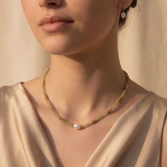 Close-up of a woman wearing a delicate gold necklace with a pearl pendant against a neutral background.