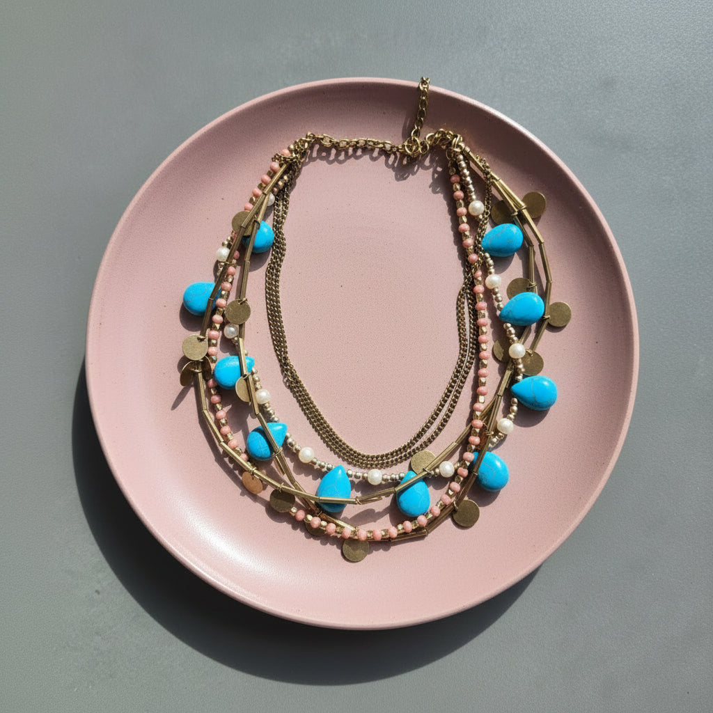 Layered necklaces with blue and gold accents on a pink plate.
