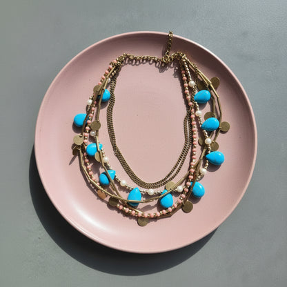 Layered necklaces with blue and gold accents on a pink plate.