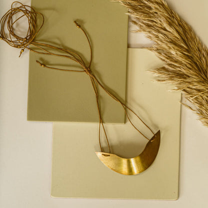 A collection of brass neckpieces with one lying flat and another coiled, alongside dried plant material and decorative papers.
